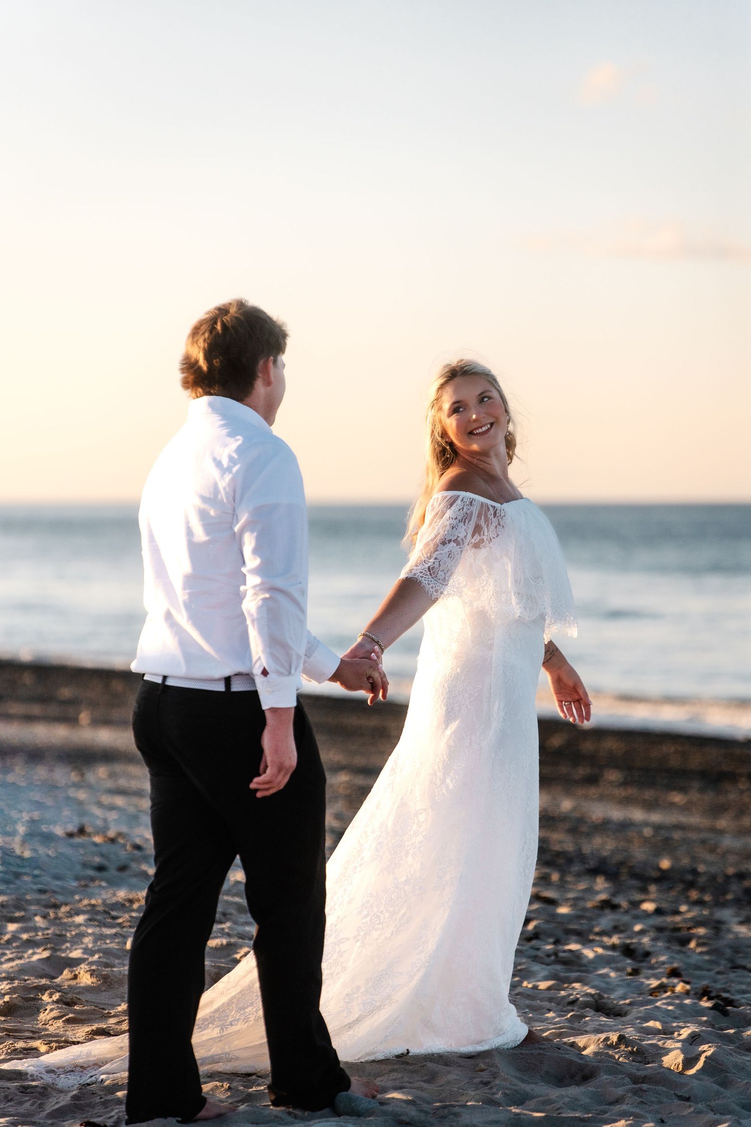 A couple holding hands on the beach at sunset, photographed by Marissa Jade Media
